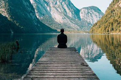 Mann sitzt achtsam auf einen Steg an einem See